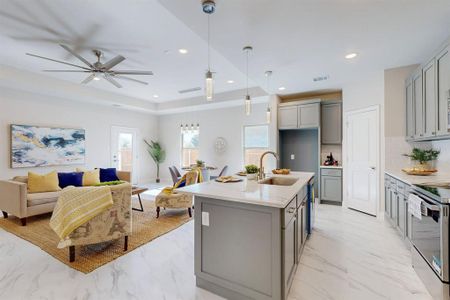 Kitchen featuring ceiling fan, a tray ceiling, a center island with sink, gray cabinetry, and sink