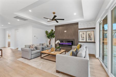 Living room featuring ceiling fan, a tray ceiling, a large fireplace, and light wood-type flooring