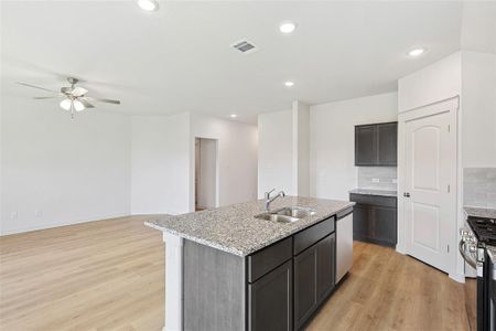 Kitchen featuring light stone counters, a kitchen island with sink, tasteful backsplash, sink, and light hardwood / wood-style flooring