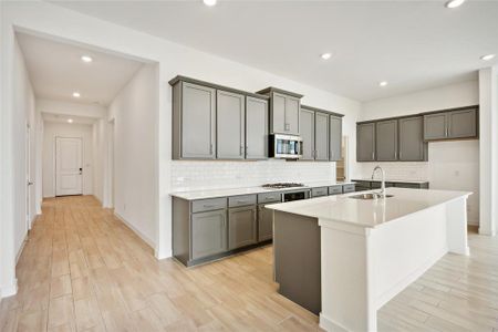 Kitchen with sink, tasteful backsplash, gray cabinets, a kitchen island with sink, and appliances with stainless steel finishes