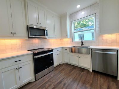 Kitchen featuring white cabinets, stainless steel appliances, dark luxury vinyl plank-style floors, and farmhouse sink