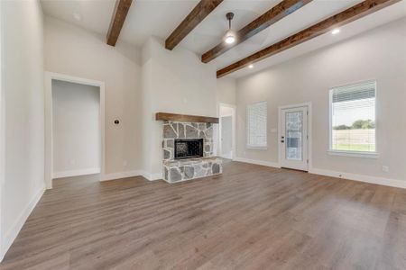 Unfurnished living room with beam ceiling, ceiling fan, a fireplace, and light hardwood / wood-style floors