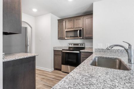 Kitchen with sink, light wood-type flooring, appliances with stainless steel finishes, dark brown cabinetry, and light stone counters