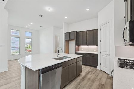 Kitchen with backsplash, light hardwood / wood-style floors, sink, a center island with sink, and stainless steel appliances