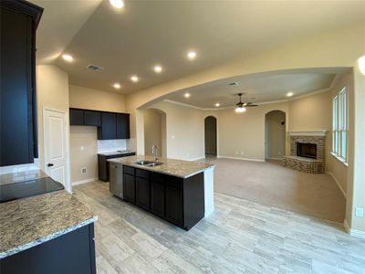 Kitchen featuring an island with sink, a brick fireplace, light stone counters, light carpet, and sink