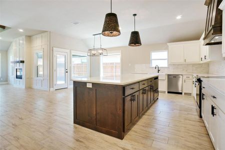 Kitchen with decorative backsplash, white cabinetry, hanging light fixtures, and appliances with stainless steel finishes