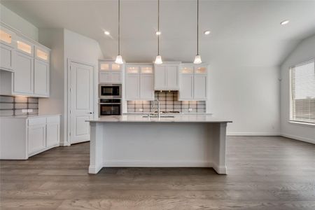 Kitchen with lofted ceiling, stainless steel appliances, white cabinets, tasteful backsplash, and wood-type flooring