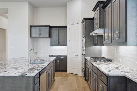 Kitchen featuring light stone countertops, appliances with stainless steel finishes, backsplash, sink, and light hardwood / wood-style floors