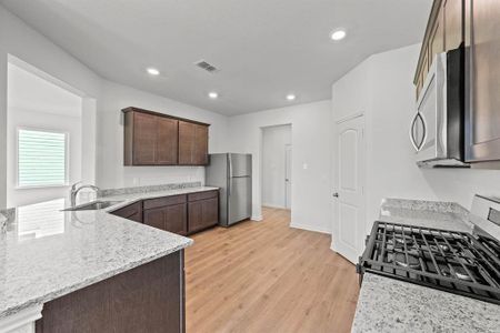 Kitchen featuring stainless steel appliances, sink, light stone countertops, dark cabinets, and light wood-style flooring