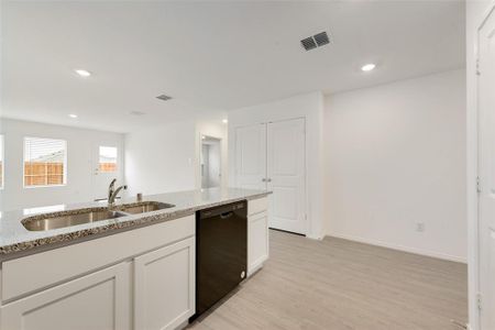 Kitchen with sink, white cabinetry, black dishwasher, light stone countertops, and light hardwood / wood-style floors