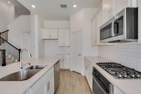 Kitchen featuring sink, light hardwood / wood-style flooring, tasteful backsplash, white cabinetry, and stainless steel appliances