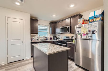 Kitchen with light stone counters, a kitchen island, light wood-type flooring, appliances with stainless steel finishes, and dark brown cabinetry