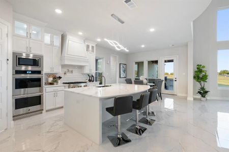 Kitchen with an island with sink, light stone counters, white cabinets, and custom exhaust hood