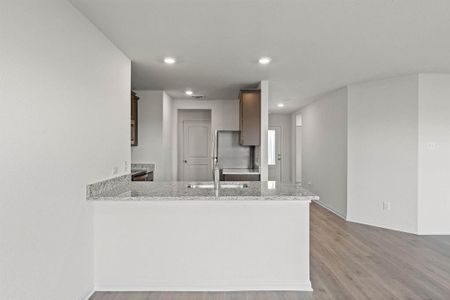 Kitchen with light wood-type flooring, sink, kitchen peninsula, and light stone countertops