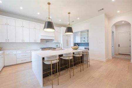 Kitchen with sink, a kitchen island with sink, white cabinetry, and light hardwood / wood-style floors