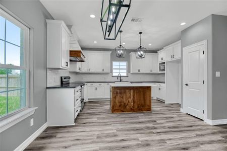 Kitchen featuring light wood-type flooring, a kitchen island, stainless steel appliances, pendant lighting, and tasteful backsplash