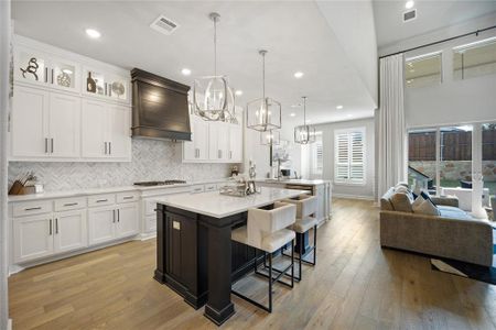 Kitchen featuring white cabinetry, custom range hood, light hardwood / wood-style flooring, and pendant lighting