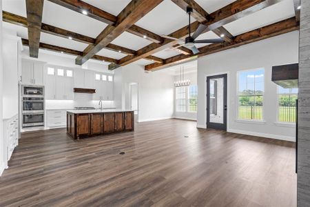 Kitchen with dark wood-type flooring, coffered ceiling, tasteful backsplash, and a kitchen island with sink