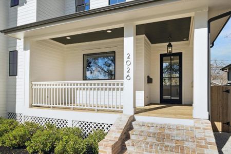 A closer look at the welcoming front porch highlights its thoughtful design and attention to detail. The classic brick steps lead to a charming wooden deck, bordered by a crisp white railing that complements the home. The modern black-framed glass front door is paired with a sleek lantern-style light fixture, creating an inviting entryway. Perfect for enjoying quiet mornings or greeting guests in style.