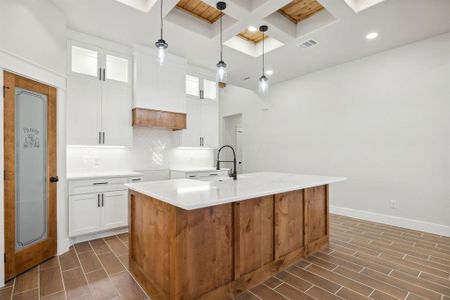 Kitchen with white cabinetry, sink, decorative light fixtures, and an island with sink