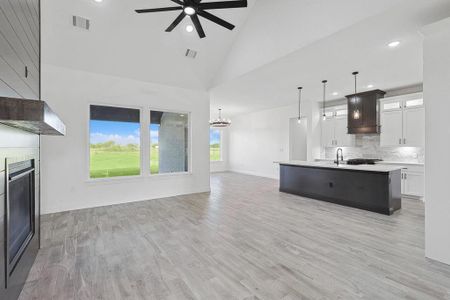 Kitchen with an island with sink, high vaulted ceiling, pendant lighting, white cabinetry, and light hardwood / wood-style flooring