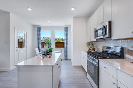 Kitchen featuring a center island, light wood-type flooring, backsplash, and appliances with stainless steel finishes