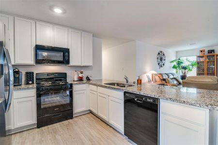 Kitchen with black appliances, white cabinetry, sink, kitchen peninsula, and light hardwood / wood-style flooring