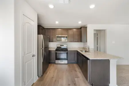 Kitchen with stainless steel appliances, sink, light stone countertops, light wood-style floors, and kitchen peninsula