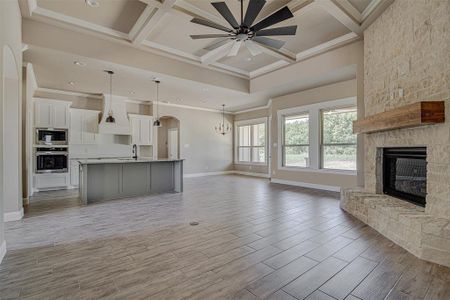 Kitchen with stainless steel appliances, an island with sink, white cabinetry, coffered ceiling, and a stone fireplace