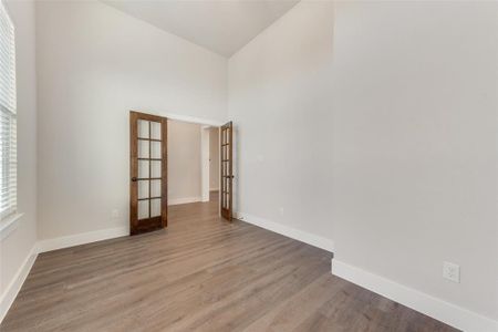 Unfurnished room featuring french doors, light wood-type flooring, and high vaulted ceiling