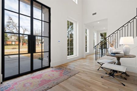 Foyer entrance featuring a high ceiling, wood finished floors, visible vents, baseboards, and stairs