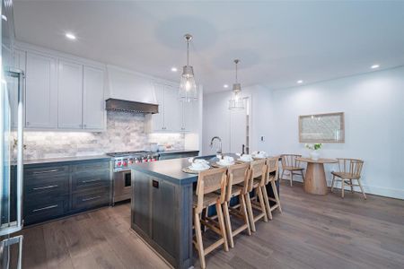 Kitchen featuring decorative light fixtures, an island with sink, white cabinets, high end stainless steel range, and custom range hood