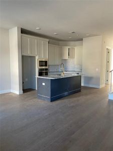 Kitchen with wood-type flooring, a center island with sink, stainless steel appliances, backsplash, and white cabinets