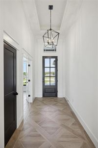 Doorway to outside featuring light parquet floors, a chandelier, and a raised ceiling