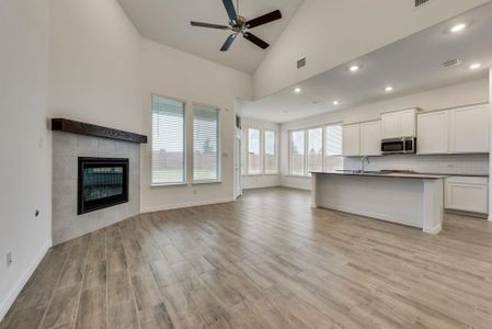 Kitchen with light hardwood / wood-style floors, high vaulted ceiling, a tiled fireplace, and white cabinetry