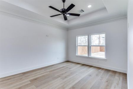 Spare room featuring a tray ceiling, visible vents, light wood-style flooring, a ceiling fan, and baseboards