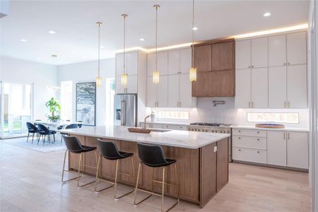 Kitchen with a center island with sink, decorative light fixtures, light wood-type flooring, backsplash, and high quality appliances