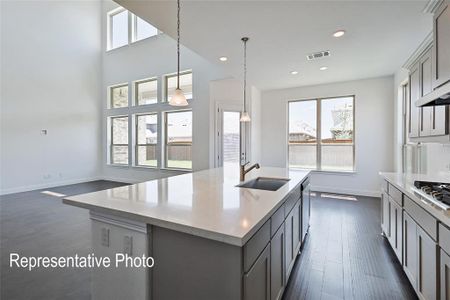 Kitchen featuring gray cabinets, decorative light fixtures, sink, a center island with sink, and dark wood-type flooring