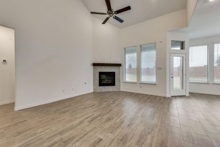 Unfurnished living room with ceiling fan, light wood-type flooring, and a high ceiling