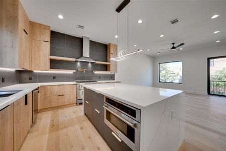 Kitchen with pendant lighting, ceiling fan, a kitchen island, light stone counters, and stainless steel appliances