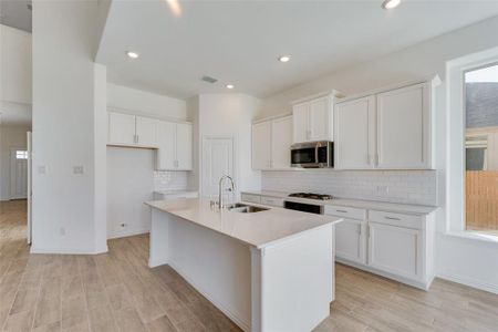 Kitchen with a center island with sink, white cabinets, sink, and light hardwood / wood-style flooring