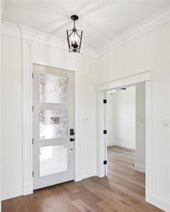 Foyer entrance featuring light wood-type flooring, crown molding, and an inviting chandelier