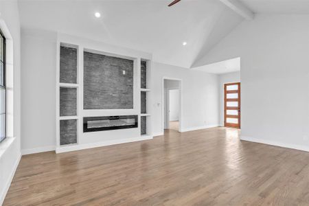 Unfurnished living room with a large fireplace, hardwood / wood-style floors, plenty of natural light, beamed ceiling, and high vaulted ceiling