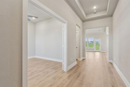 Hallway with light wood-type flooring and a tray ceiling