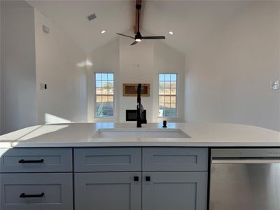 Kitchen featuring vaulted ceiling, gray cabinets, stainless steel dishwasher, and ceiling fan