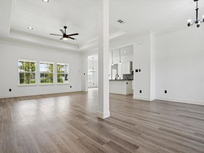 Unfurnished living room featuring ceiling fan with notable chandelier, light wood-type flooring, sink, and a raised ceiling