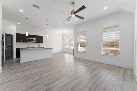 Unfurnished living room featuring ceiling fan with notable chandelier, light hardwood / wood-style floors, and sink