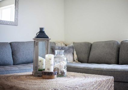 Staged living room with grey couch and white colored coffee table with vase and candle sitting on it.