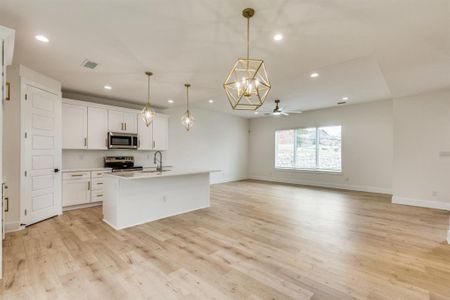 Kitchen featuring white cabinetry, decorative light fixtures, a kitchen island with sink, ceiling fan with notable chandelier, and appliances with stainless steel finishes