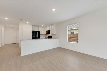 Kitchen featuring white cabinetry, light stone counters, light hardwood / wood-style flooring, kitchen peninsula, and black appliances